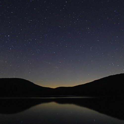 An astrophotography image of the night sky with stars and a lake
