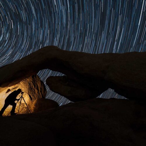 A photographers' silhouette against a rock formation photographing the stars with long exposure.