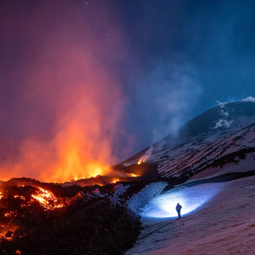 Earth's elements of fire and ice converge at night on the snowy mountain of Mt Etna, Italy.