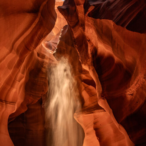 Upper Antelope Canyon in northern Arizona, USA with narrow sandstone passageway and wavy walls, magical light beams and sunbeam effects are shining through the cracks above and catching falling sand.