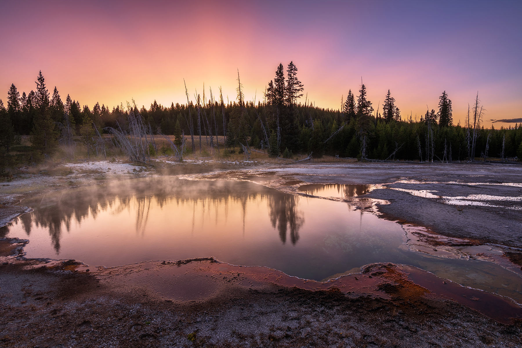 Yellowstone National Park, Wyoming Abyss Pool reflects the vibrant pinks and oranges of the sky during a colorful sunset in the West Thumb Geyser Basin.