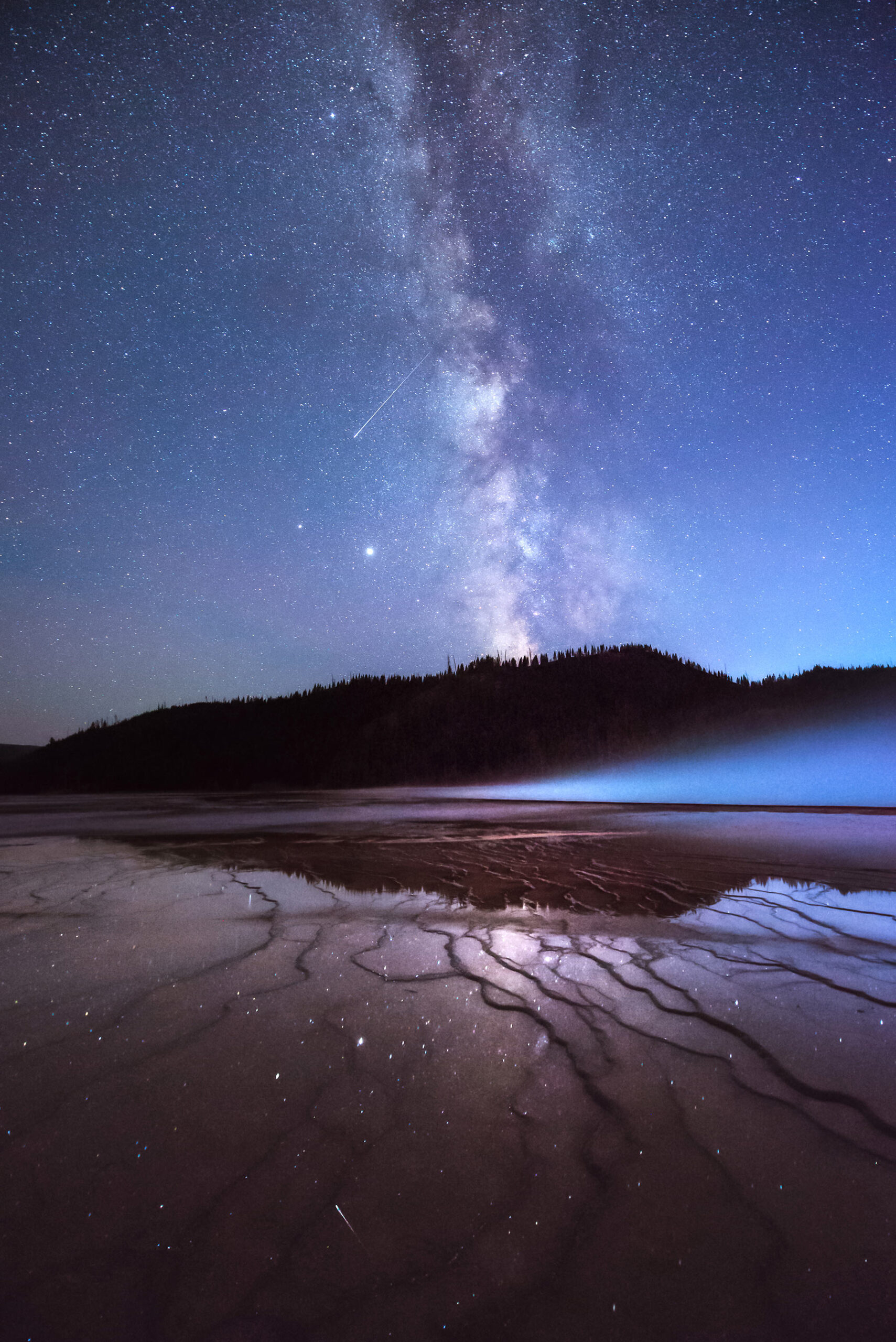 Yellowstone National Park, Wyoming The Milky Way stretches across the night sky and reflects, along with a meteor and stars, onto the terraces of Grand Prismatic Spring.