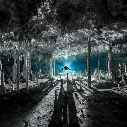 A cave diver hovers inside a vast flooded chamber, surrounded by ancient formations within the Greater Mayan Aquifer, Mexico’s hidden freshwater world.